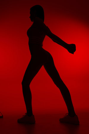 Silhouette of a woman sport fitness stretching against a vibrant red background, showing athletic posture and strength in minimalist lighting and dynamic pose.の写真素材