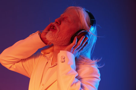 Elderly man enjoying music with headphones, vibrant blue and orange lighting, expressive emotions, stylish white suit, dynamic concept of music and joy, timeless enjoyment of soundの写真素材