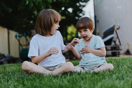 Happy children playing together outdoors, enjoying a sunny day with laughter and joy. The vibrant green grass adds to the cheerful atmosphere of the scene.の写真素材