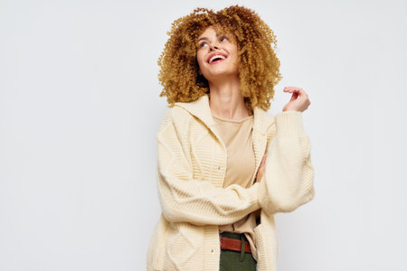 Happy woman smiling in a cozy outfit, medium length curly hair, light cardigan, standing against a...
