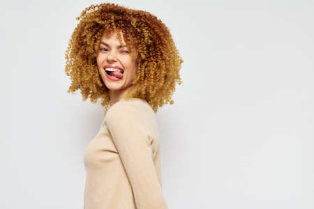 Happy woman with curly hair playfully sticking out her tongue against a neutral background, showcasing a lively and confident expression, perfect for cheerful conceptsの写真素材