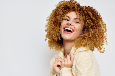 joyful woman with curly hair, smiling brightly against a light background, exuding happiness and positive energy in cozy outfit, expressive emotions captured in close upの写真素材