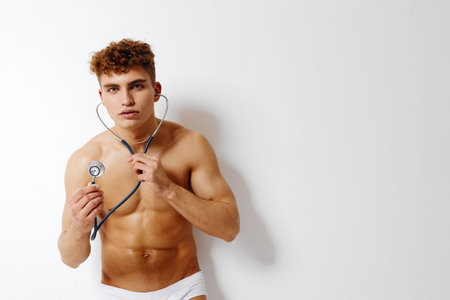 Young male medical professional in underwear holding stethoscope, showcasing a confident expression, against a minimalistic white background. Health and wellness concept.の写真素材
