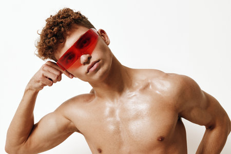 Confident shirtless young man posing with red sunglasses, showcasing a strong physique against a neutral background. Fashion and self-expression concept.の写真素材