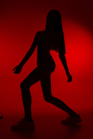 Silhouette of a woman sport fitness exercising in dynamic pose against vibrant red background, emphasizing strength, motion, and athleticism in a modern studio setting.の写真素材