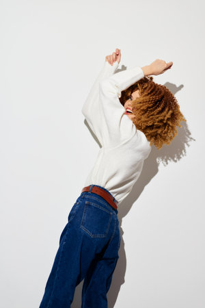 Cheerful young woman dancing against a plain white background, showcasing curly hair and casual...