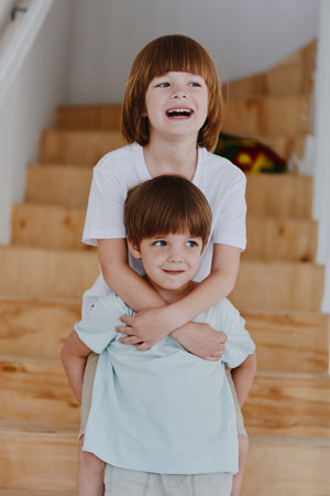 Two playful boys share a joyful moment, one laughing while being playfully carried. Their...