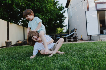 Playful children enjoying a sunny day outside, displaying joy and laughter while playing together in the green grass of the backyard.の写真素材