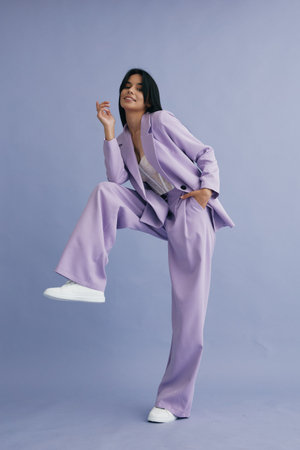 stylish woman wearing a lilac suit and white sneakers posing confidently against a soft purple backdrop, showcasing modern fashion and a joyful expressionの写真素材