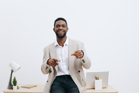 Smiling man in business casual attire, sitting at a modern office desk with a laptop, minimal decor, white background, relaxed and confident mood, suitable for corporate or professional concepts.の写真素材
