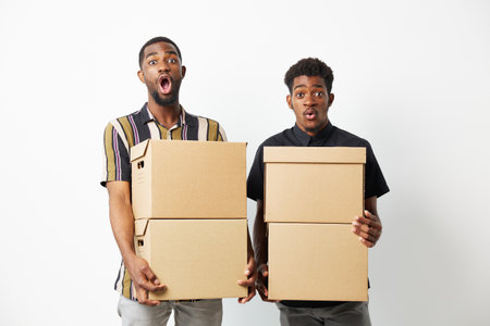 Two surprised African American men holding cardboard boxes showcase excitement and curiosity,...