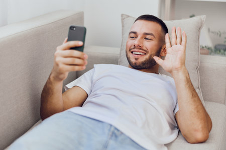 Smiling man enjoying a video call, representing the blend of personal and work life. His casual attire and relaxed position reflect modern communication trends.の写真素材