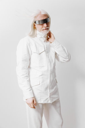 Futuristic fashion portrait of a model with white hair and sunglasses in a white outfit against a...