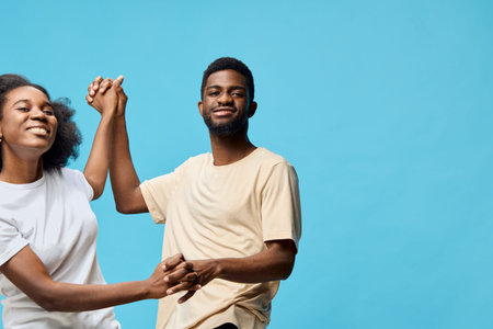 Happy young couple dancing together against a bright blue background, expressing joy and love through playful interactions in casual clothingの写真素材