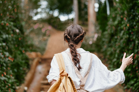 Young woman walking through a lush garden, wearing a white shirt and brown overalls, conveying a sense of peace and connection with natureの写真素材