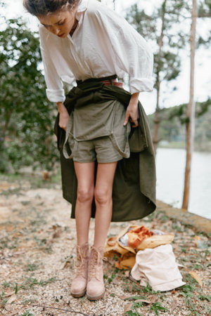 Young woman in nature adjusting her outfit reflects a casual, outdoor lifestyle with earthy tones and an adventurous spirit, showcasing a connection with natureの写真素材
