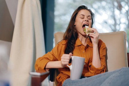 Young woman enjoying a healthy snack while relaxing at home, wearing a stylish orange shirt,...