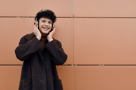 Fashionable young man listening to music with headphones against an orange wall background