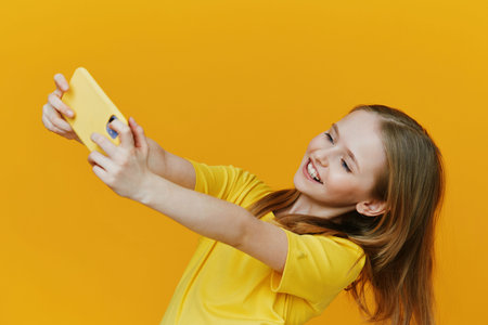 Happy young girl taking a selfie against a bright yellow background, wearing a cheerful yellow t shirt, expressing joy and excitement in a vibrant, playful settingの写真素材