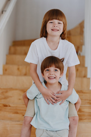Two cheerful boys playing on wooden stairs, showcasing their joy and strong bond. This charming scene perfectly captures childhood happiness.の写真素材
