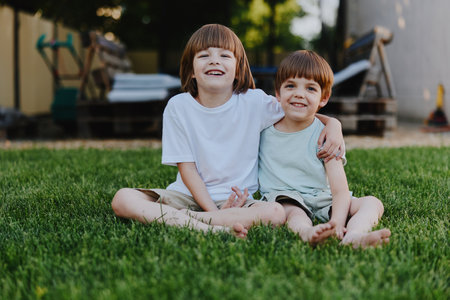 Smiling boys enjoying a sunny day, sharing a moment of friendship on a grassy lawn, radiating joy and innocence in a relaxed outdoor setting.の写真素材