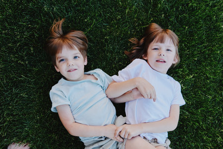 Playful children lying on grass, enjoying a sunny day. Their expressions reflect happiness and innocence, creating a cheerful atmosphere.の写真素材