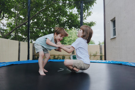 Two joyful children jumping together on a trampoline, showcasing excitement and playfulness in a sunny backyard environment.の写真素材