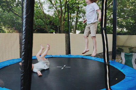 Happy kids jumping on a trampoline, enjoying playful moments in the sunny backyard, filled with laughter and excitement, showcasing childhood joy.の写真素材