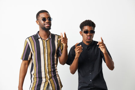 Two stylish black men wearing sunglasses pose confidently against a white background, embodying...