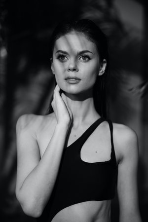 Monochrome image of a woman in swimsuit standing by palm tree on beachの写真素材