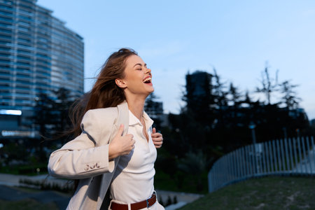 Confident businesswoman enjoying a moment outdoors in a professional outfit, exuding joy and empowerment in an urban setting with a modern background.の写真素材