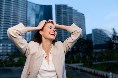 Energetic businesswoman celebrating success in an urban setting, wearing a stylish blazer and exuding joy with a modern cityscape backdrop.の写真素材