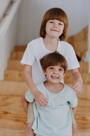 Smiling brothers joyfully playing together on wooden stairs, showcasing their bond and happiness in a bright and cheerful environment.の写真素材
