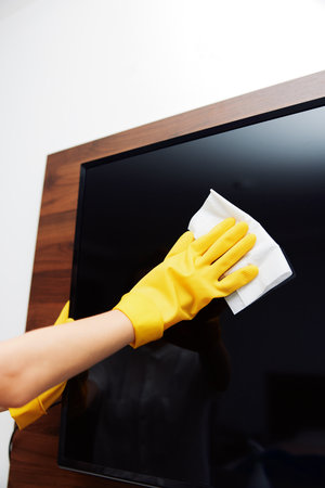 Woman in rubber gloves cleaning tv screen with cloth and yellow glove on arm of tv standの写真素材