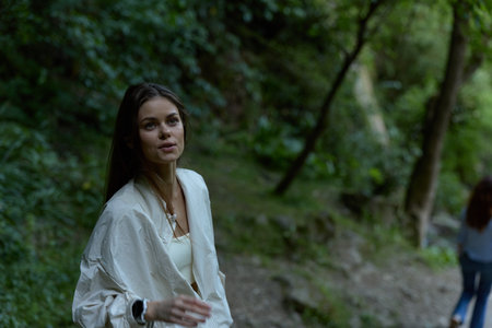 young woman in white jacket walking through lush green forest, natural light highlighting her...