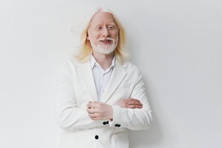 Portrait of a smiling middle aged man with long light hair and a white beard, wearing a stylish white suit against a clean, minimalistic light backgroundの写真素材