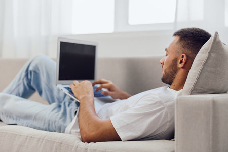 Relaxed man working on a laptop at home, showcasing modern lifestyle, creativity, and productivity in a cozy atmosphere. Ideal for remote work themes.の写真素材