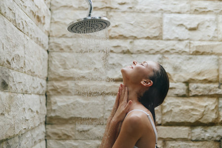 Young woman enjoying outdoor shower with warm water, natural stone wall background, peaceful...