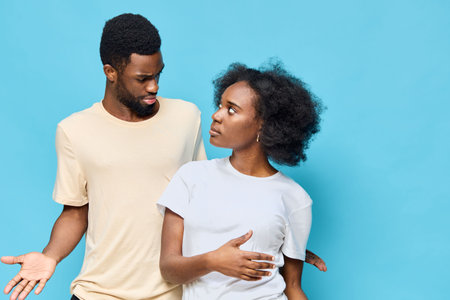 A couple expressing mixed emotions, showcasing a conversation about relationship challenges, with a vibrant blue background complementing their casual attireの写真素材