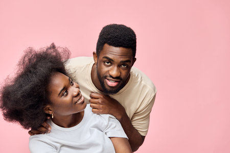 Happy young African couple posing together with playful expressions against a soft pink background, showcasing natural hair and stylish casual wearの写真素材