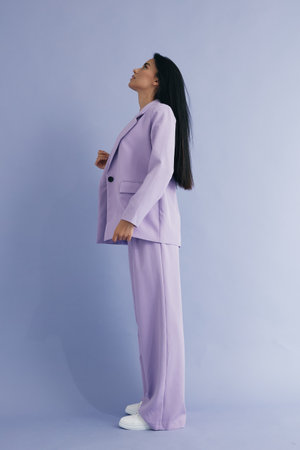 woman in lavender suit standing sideways against soft purple background with natural long hair, casual white sneakers, minimalistic and modern styleの写真素材