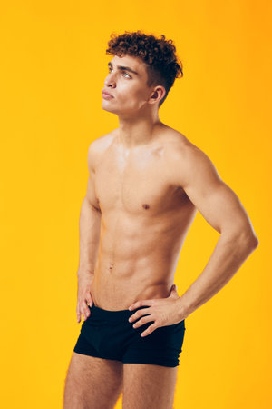 Athletic young man posing confidently against a vibrant yellow background, showcasing toned physique, reflecting strength and fitness.の写真素材