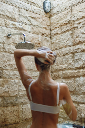 woman showering outdoors with soap, stone wall background, natural light, wet hair, relaxing moment,...
