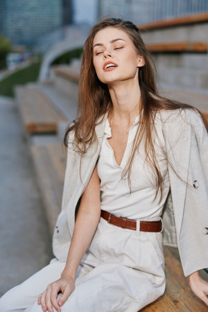 Businesswoman in stylish outfit exuding confidence and elegance, seated outdoors with a modern urban backdrop showcasing her professional demeanor and relaxed expression.の写真素材