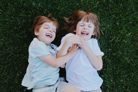 Two joyful children playing on green grass, laughing and smiling together, capturing the essence of...
