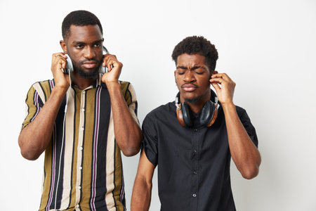 Stylish black men listening to music with headphones, showcasing emotions of concentration and...
