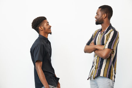 Two black men engaged in conversation, sharing smiles and laughter. The photo captures a moment of friendship against a clean white background.の写真素材