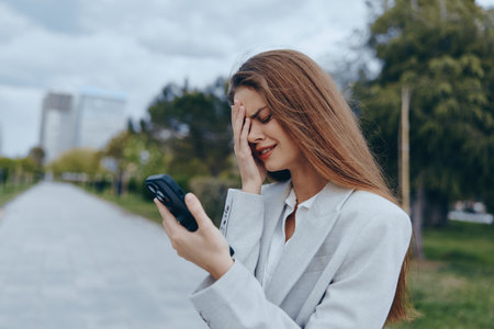 frustrated woman holding smartphone outdoors in gray blazer feeling stressed about finance and...