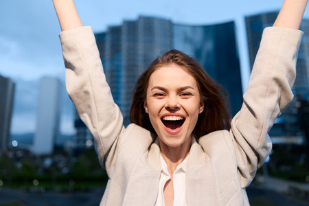 Confident woman in business attire celebrating success against a city skyline.の写真素材