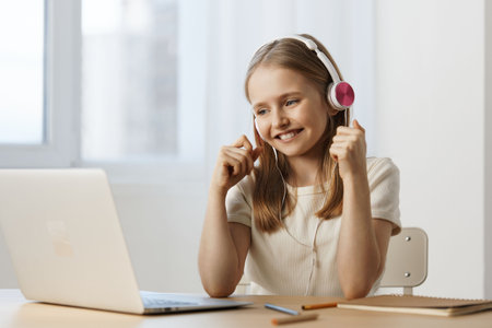 Happy girl with headphones enjoying online learning at home, bright colors and modern decor reflecting a cheerful atmosphereの写真素材
